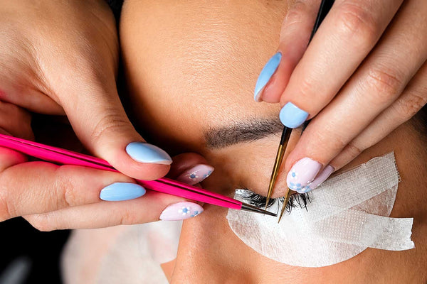 Professionele wimperextensions applicatie met pastel blauwe nail art en nauwkeurige isolatie techniek.